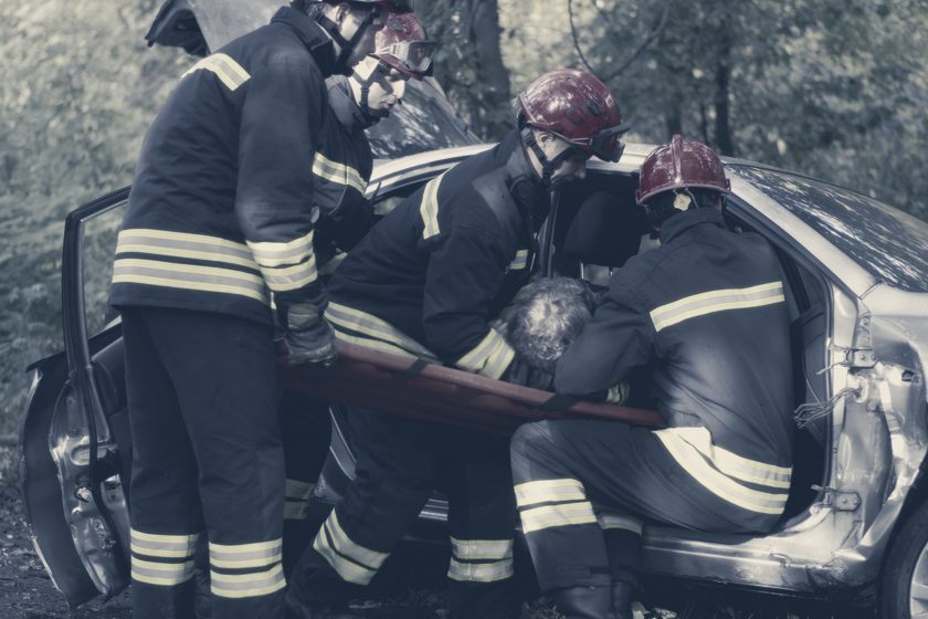 Firefighters lifting a crash victim clear of a wrecked car